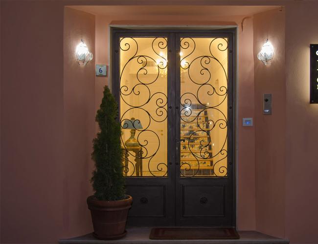 Ingresso illuminato di un B&B con porta in ferro battuto e insegna luminosa.