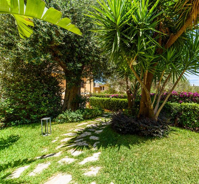 Giardino verde con sentiero, piante rigogliose e cielo sereno.