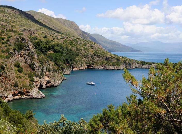 Una baia rocciosa con acque turchesi e barche ancorate, circondata da colline verdi.