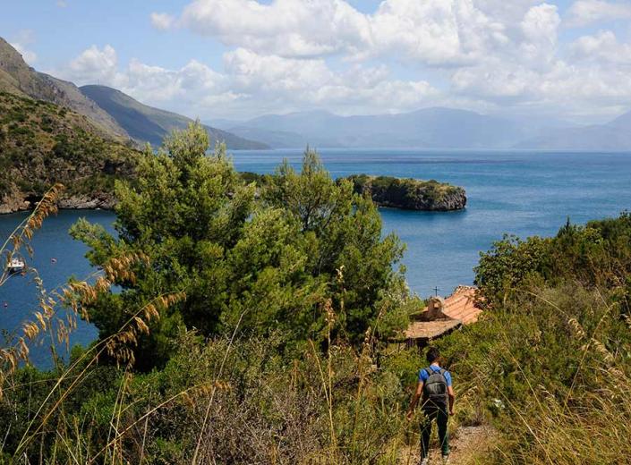 Hiker on coastal path with sea and island view.