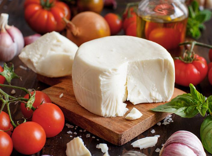 Cheese on a board with tomatoes, basil, and garlic.