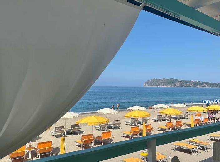 Spiaggia affollata con ombrelloni colorati, mare blu e scogliere imponenti sullo sfondo.