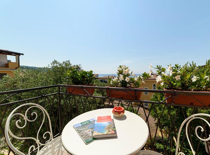 Balcone con vista mare, piante fiorite e libri su un tavolo rotondo.